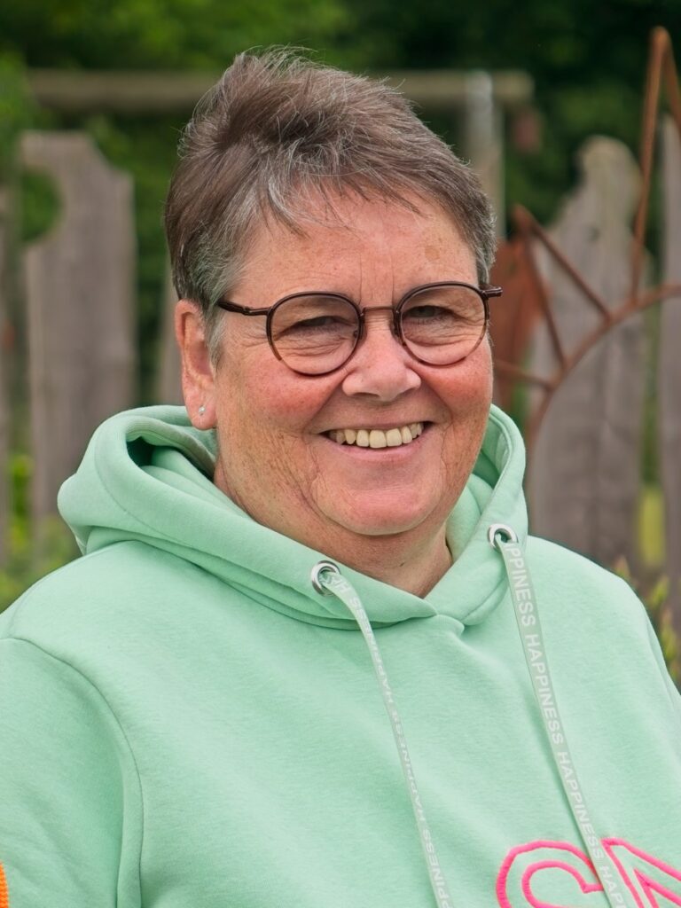 Portrait einer freundlich lächelnden Person im Grünen mit Brille und mintgrünem Kapuzenpullover.