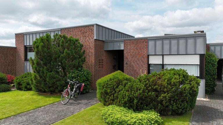 Flachdachbungalow mit moderner Fassadensanierung in Stehfalzoptik – Prefa P.10 hellgrau, Klinkerfassade und gepflegter Vorgarten