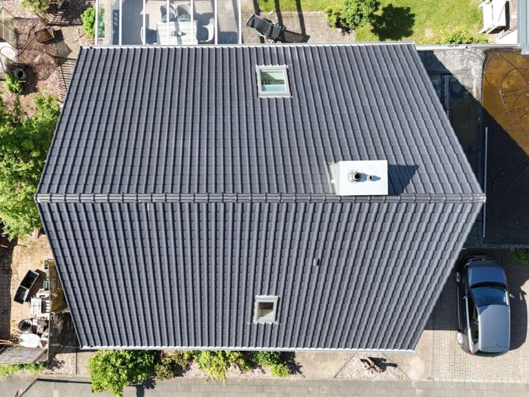 Draufsicht auf ein neu gedecktes Satteldach mit dunkelgrauen Dachziegeln, Dachflächenfenstern und Schornstein.