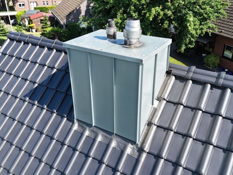 Nahaufnahme eines Schornsteins mit Scharen aus vorbewittertem Rheinzink auf einem neu gedeckten Dach mit dunkelgrauen Laumans-Ziegeln.