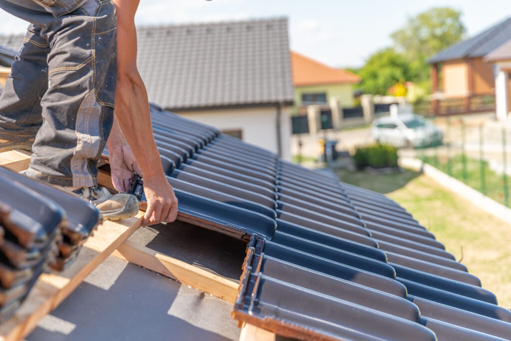 Dachdecker bei der Montage von dunkel glänzenden Tondachziegeln auf einem Steildach in Kevelaer – präzise Handarbeit beim Eindecken eines Wohnhausdachs.